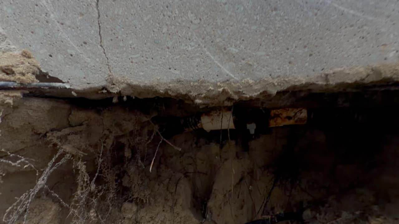 Excavated ground beneath the edge of a concrete slab, exposing a buried pool line and its fittings