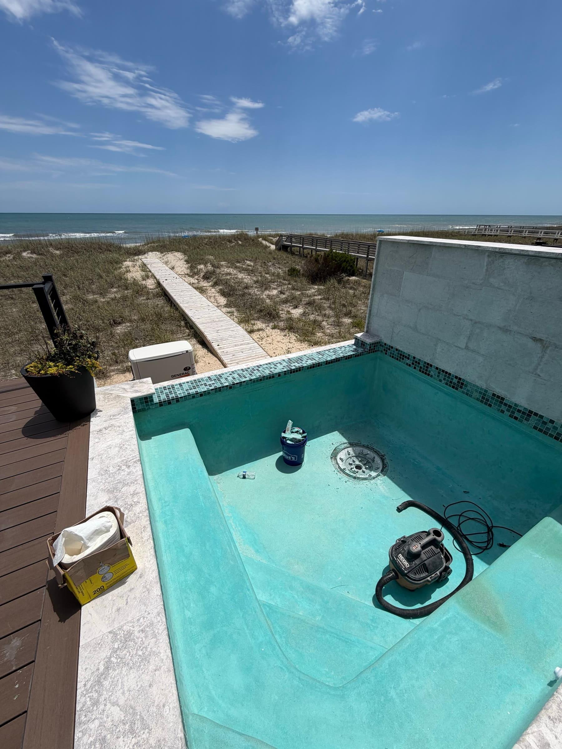 An oceanfront plunge pool mid-service, beach boardwalk and dunes beyond