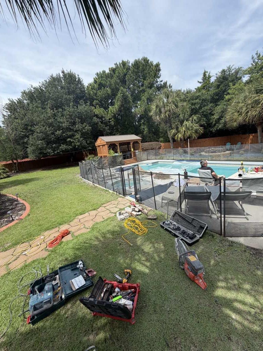 Open tool cases on grass beside a screened pool enclosure, with coiled hoses and a saw laid out
