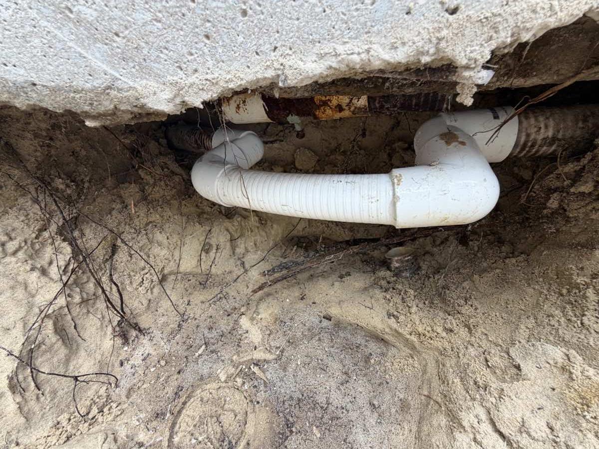 The same excavation after repair, with a new white PVC section spliced into the original line