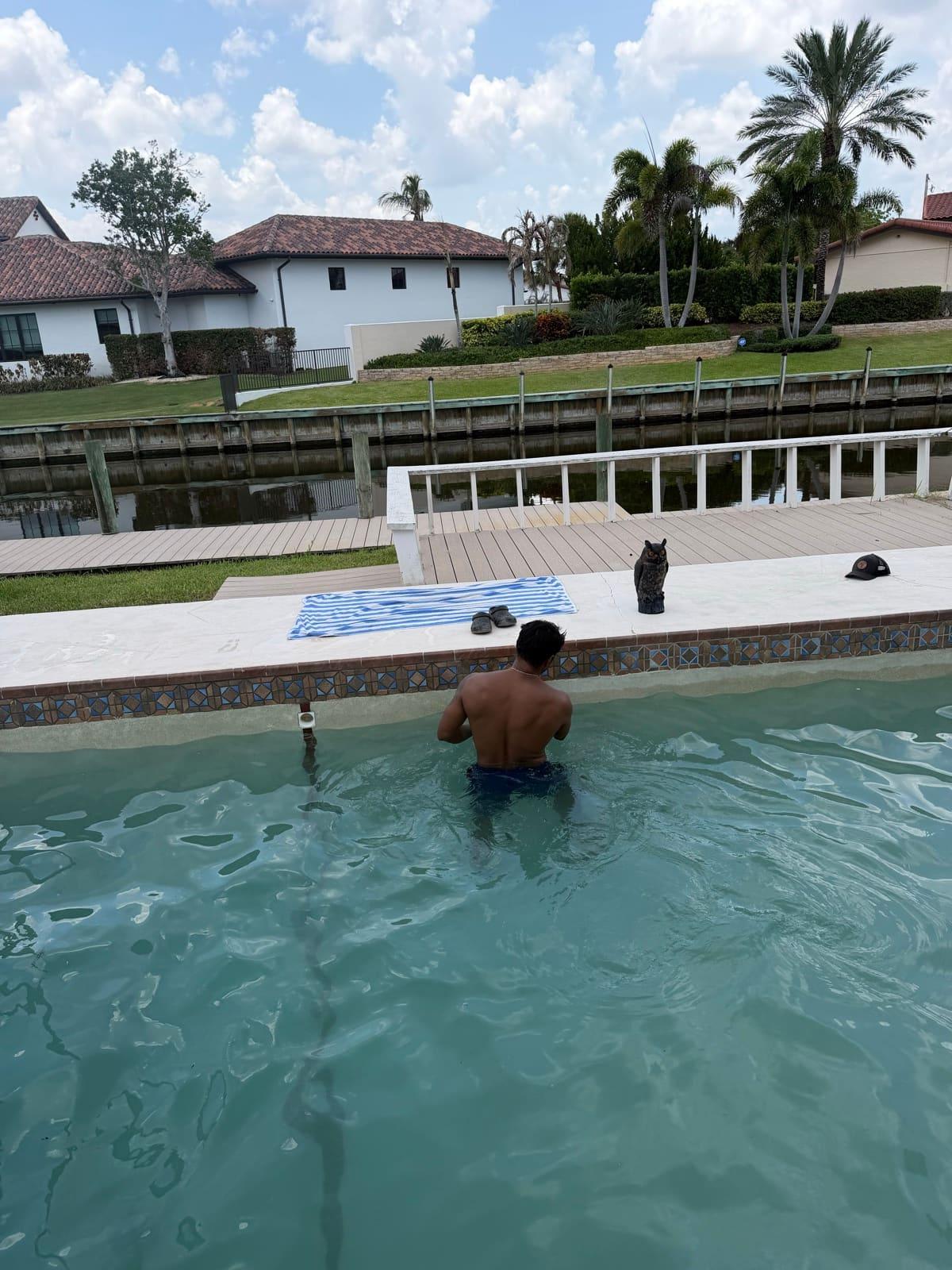 A technician working chest-deep at the tile line of a canal-front pool