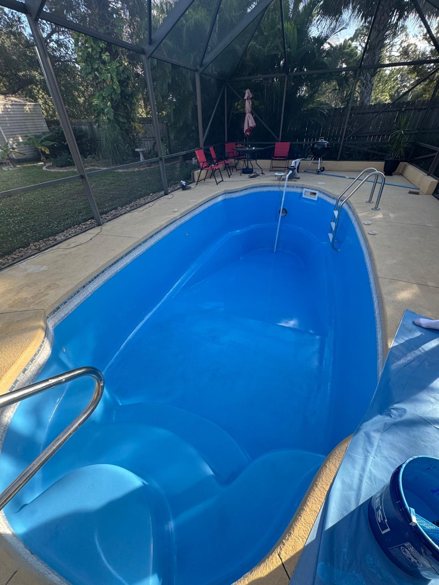 A drained bright blue fiberglass pool shell inside a screened enclosure, with a chrome handrail at the steps