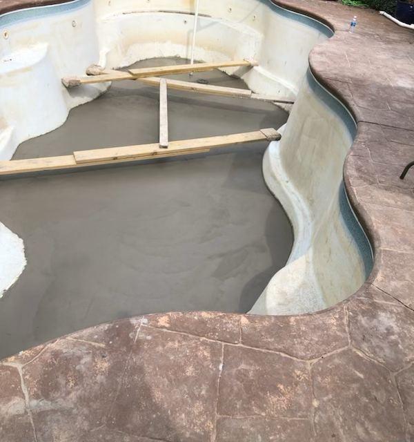 A drained freeform pool part-way through resurfacing, with a fresh mortar floor and boards laid across it