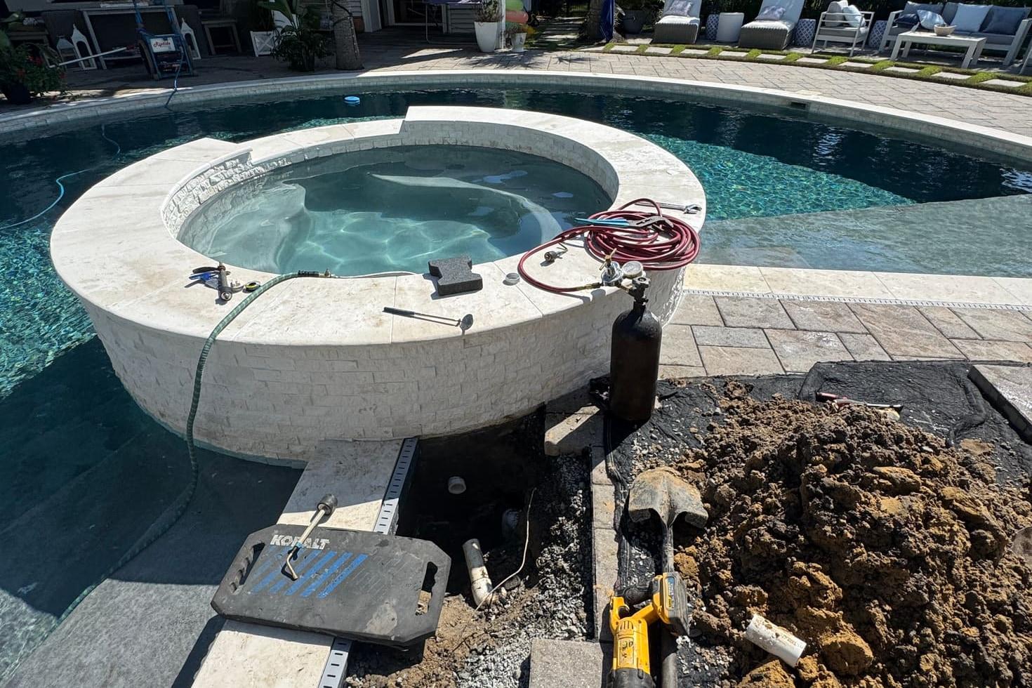 Targeted deck excavation beside a raised spa, with pressure-testing equipment and tools laid out on the pool deck.