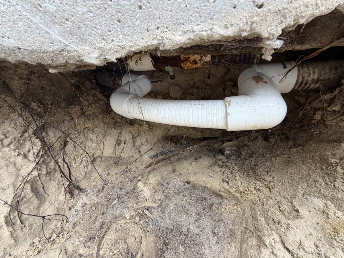The same excavation after repair, with a new white PVC section spliced into the original line