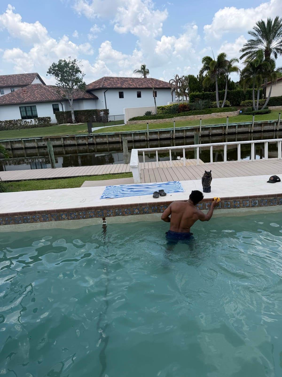 A technician scrubbing the waterline tile of a canal-front pool by hand