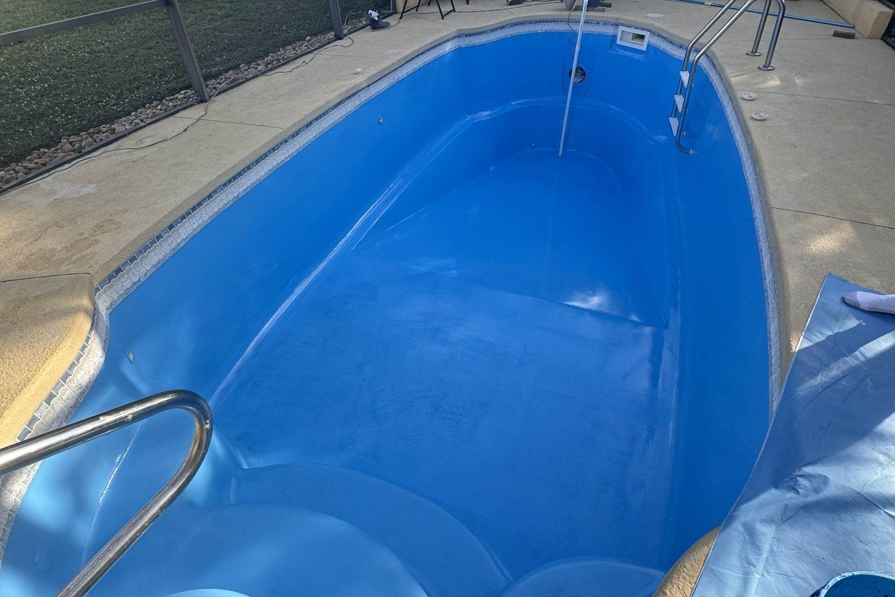 A drained bright blue fiberglass pool shell inside a screened enclosure, with a chrome handrail at the steps