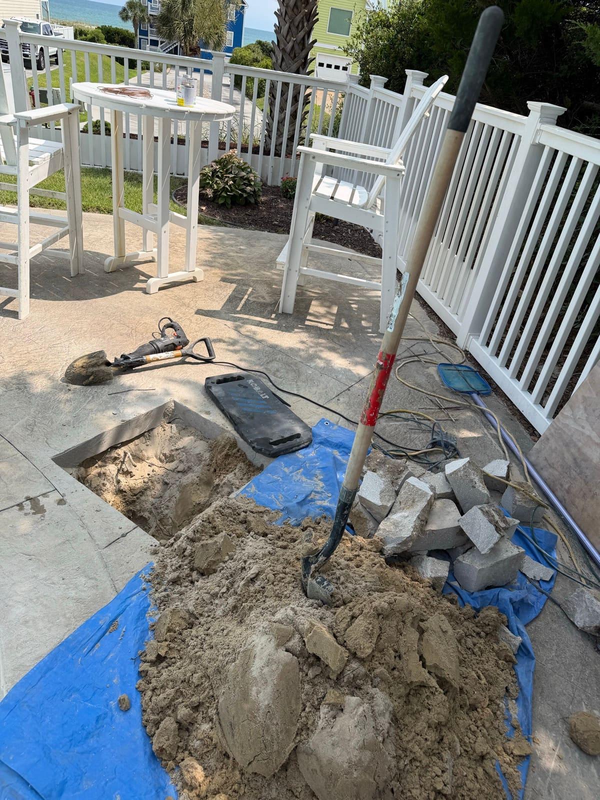 A small opened section of pool deck with neatly cut concrete blocks stacked on a tarp and a jackhammer set down